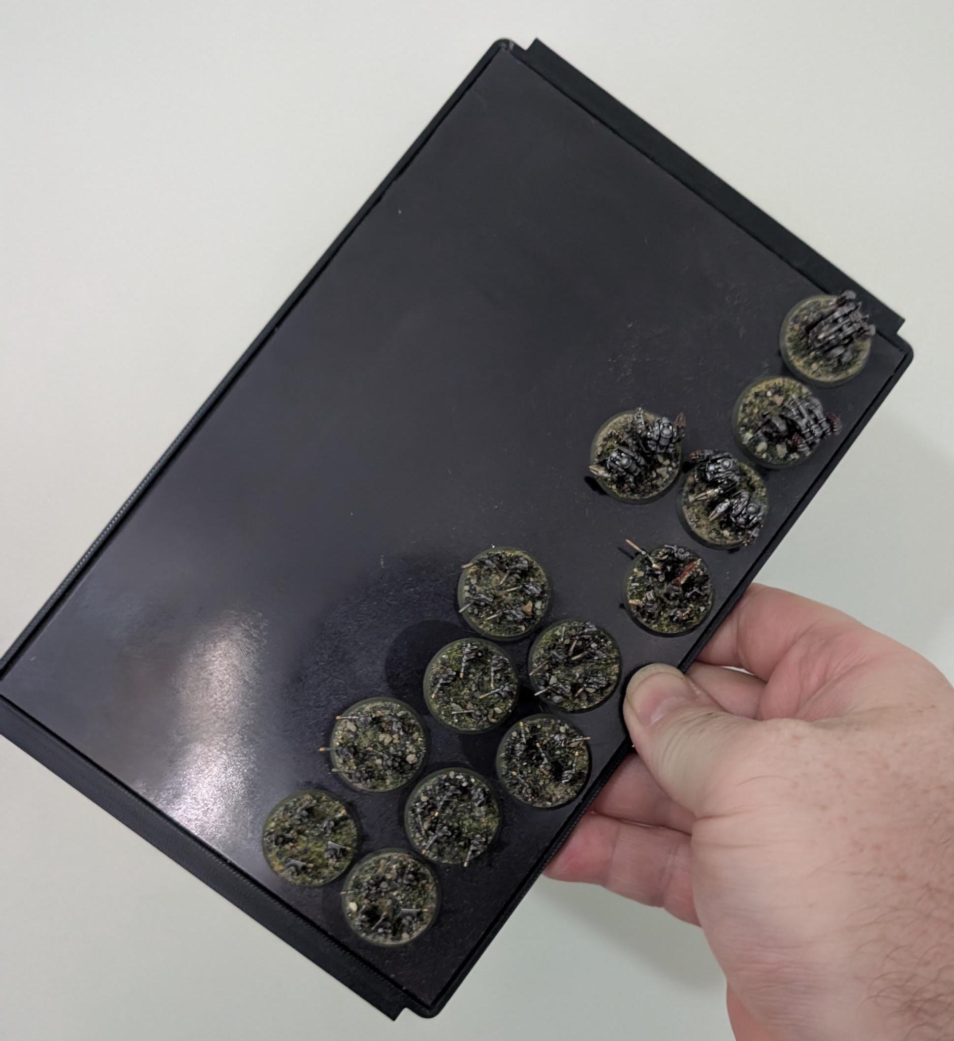 Hand holding a miniatures carrying case containing various detailed game miniatures for easy transport